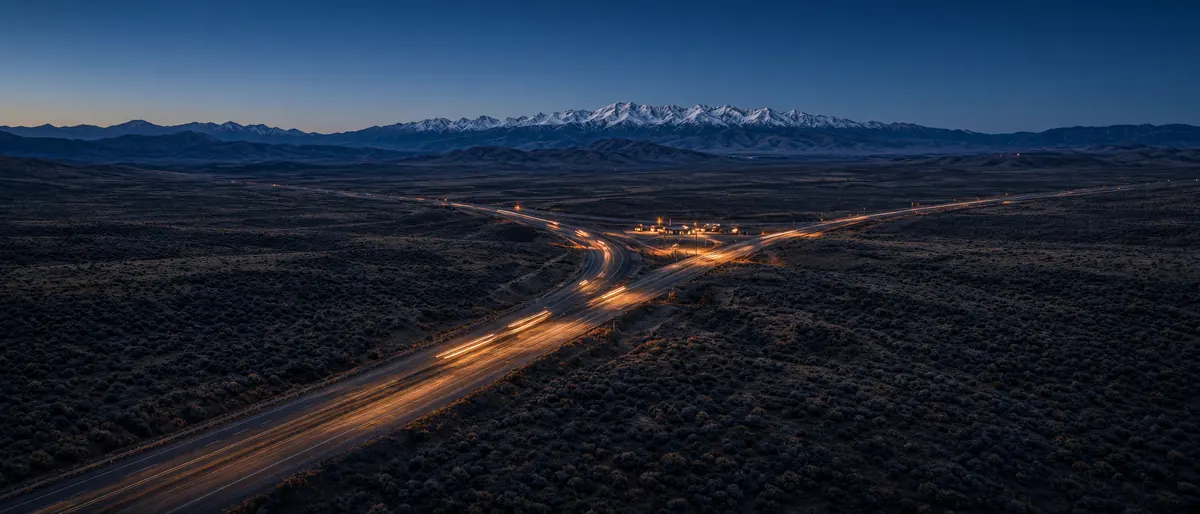 Highway crossing high desert toward snowy mountains at dusk