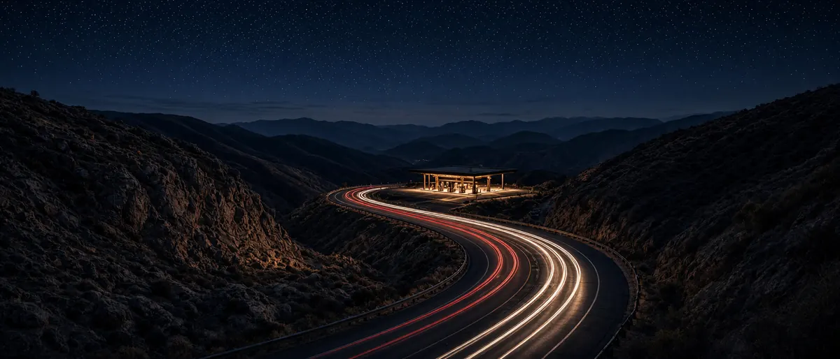 Mountain highway at night with light trails leading to a lit charging station